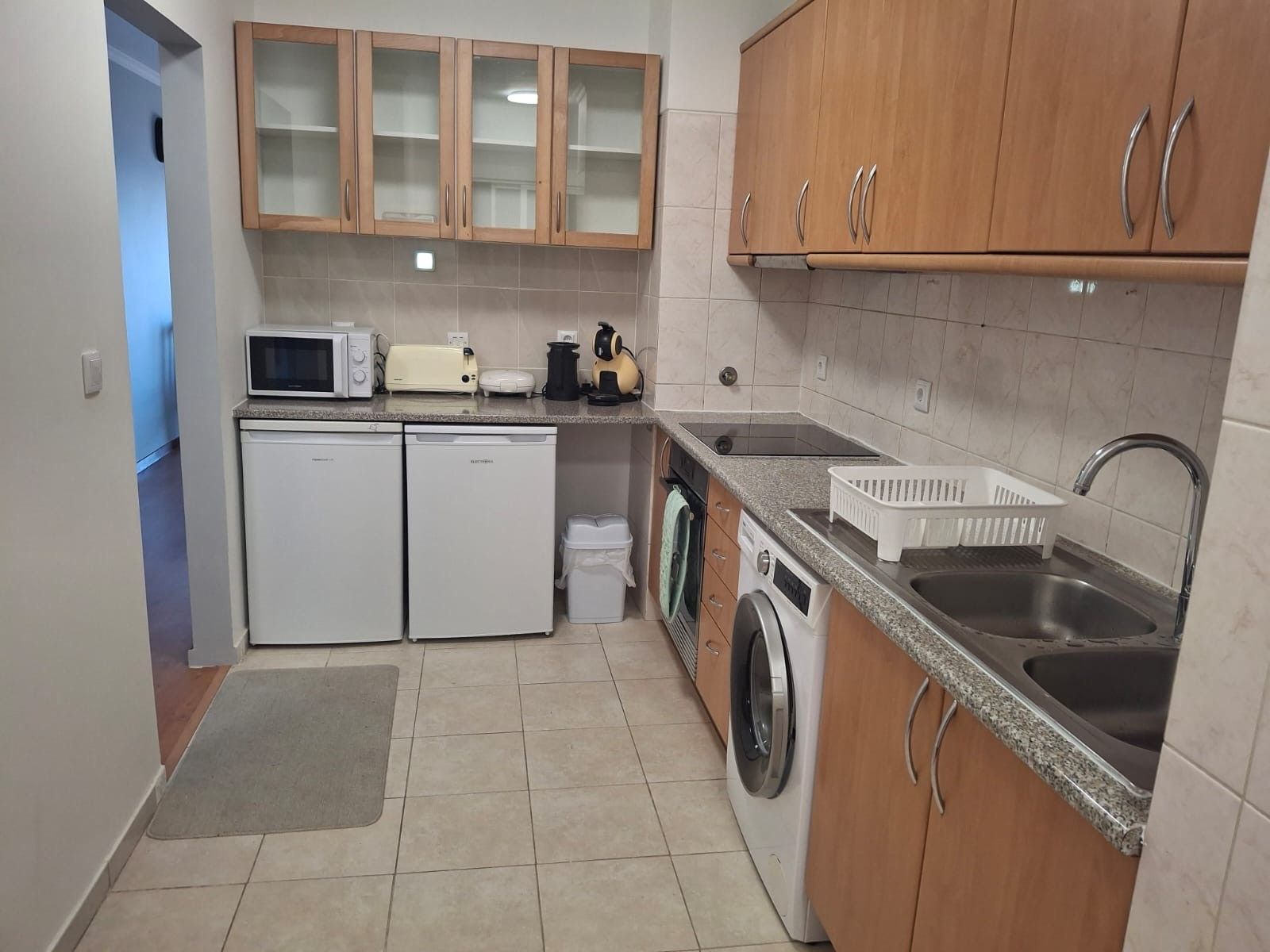 A compact kitchen with a microwave, toaster, washing machine, and a sink.