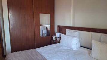 A hotel room with a large bed, a wooden wardrobe, a nightstand with a lamp, and a mirror.