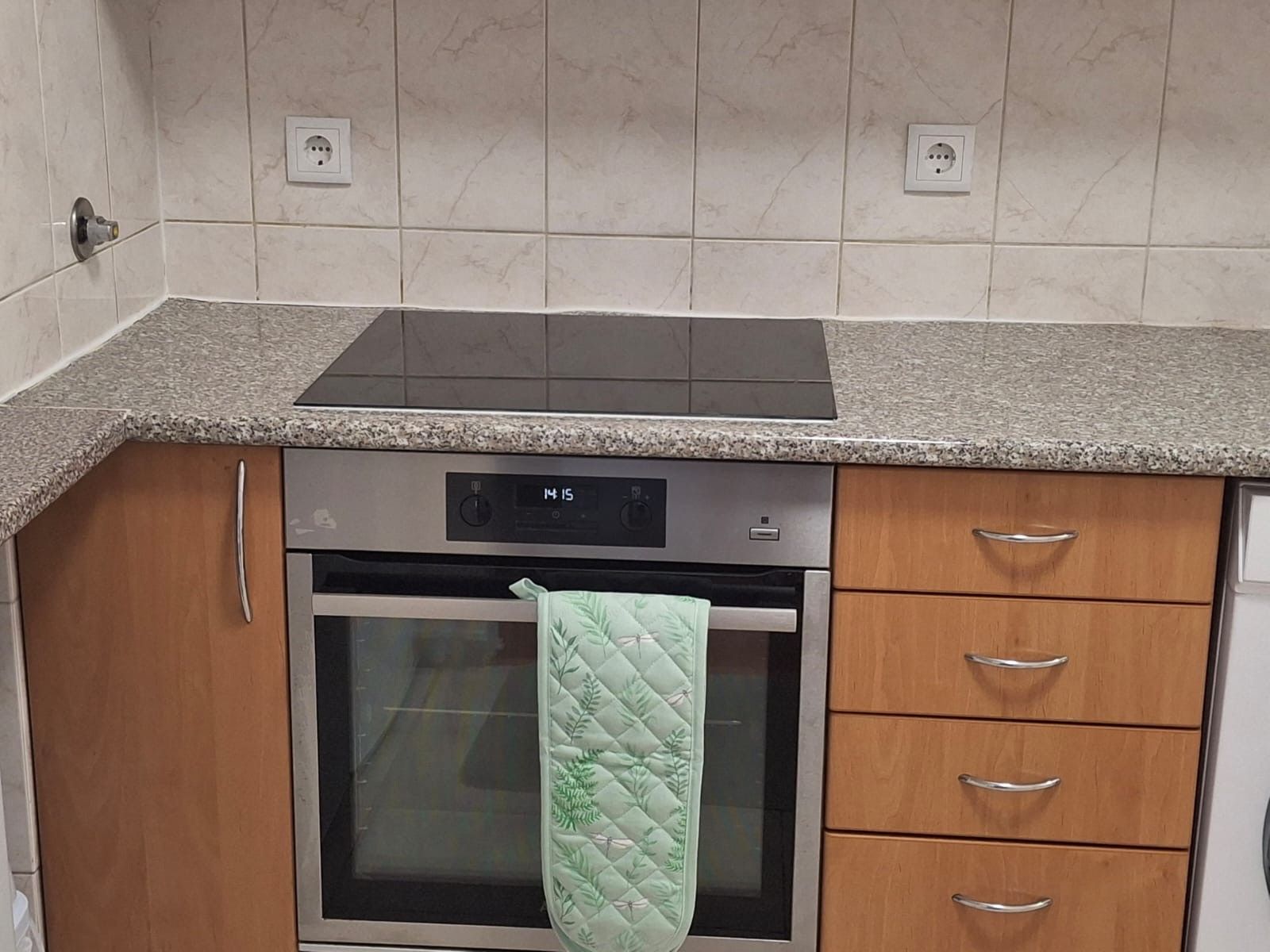 A kitchen with a built-in oven, a digital clock, and a granite countertop.