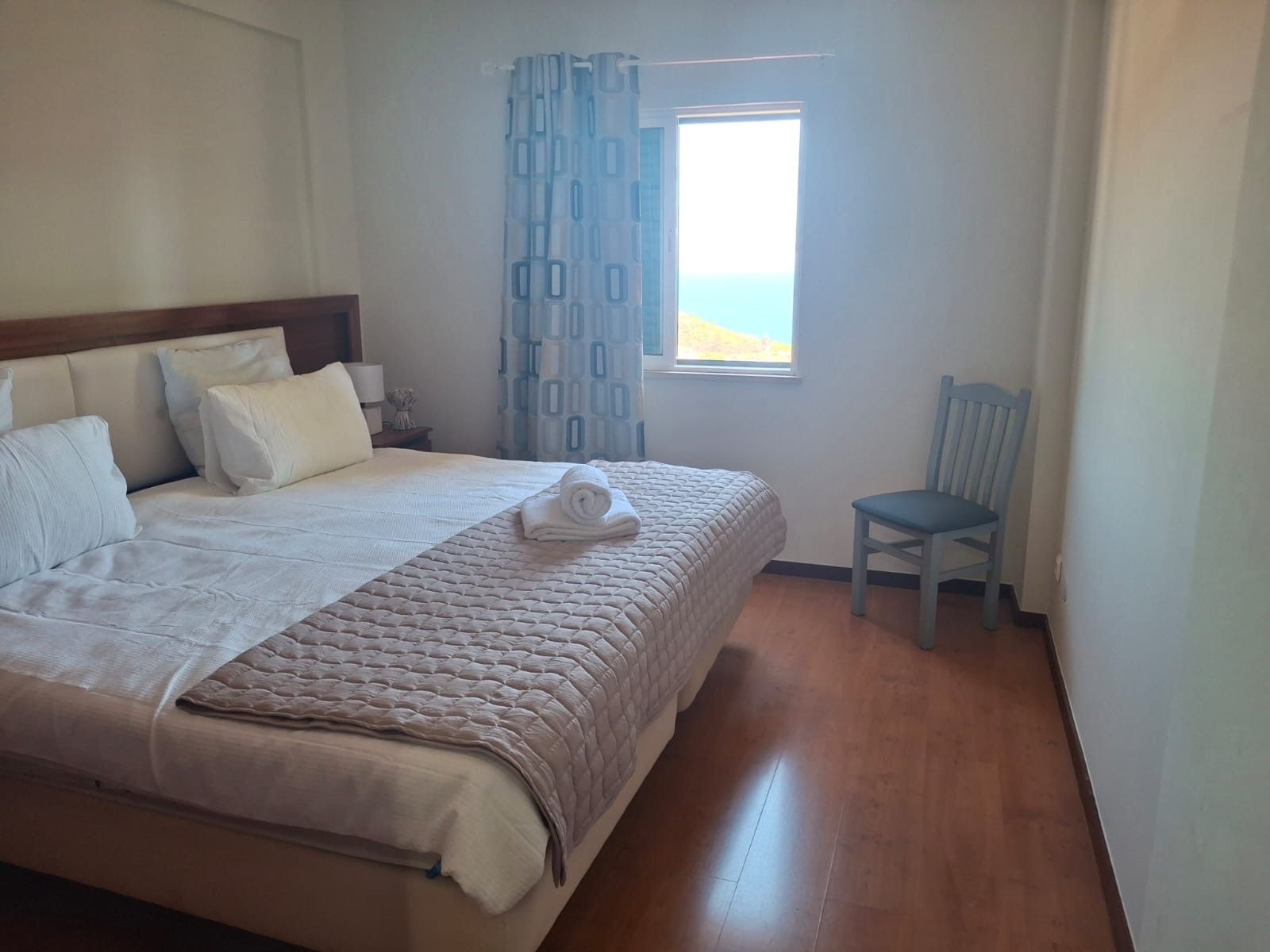 A hotel room with a bed, a chair, a window, and a view of the sea.