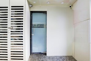 A door with a metal handle and a glass panel, a white wall, and a ceiling with recessed lighting.