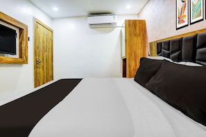 Ein Hotelzimmer mit einem Bett, einer Holztür, einer Klimaanlage und einem gerahmten Bild an der Wand.