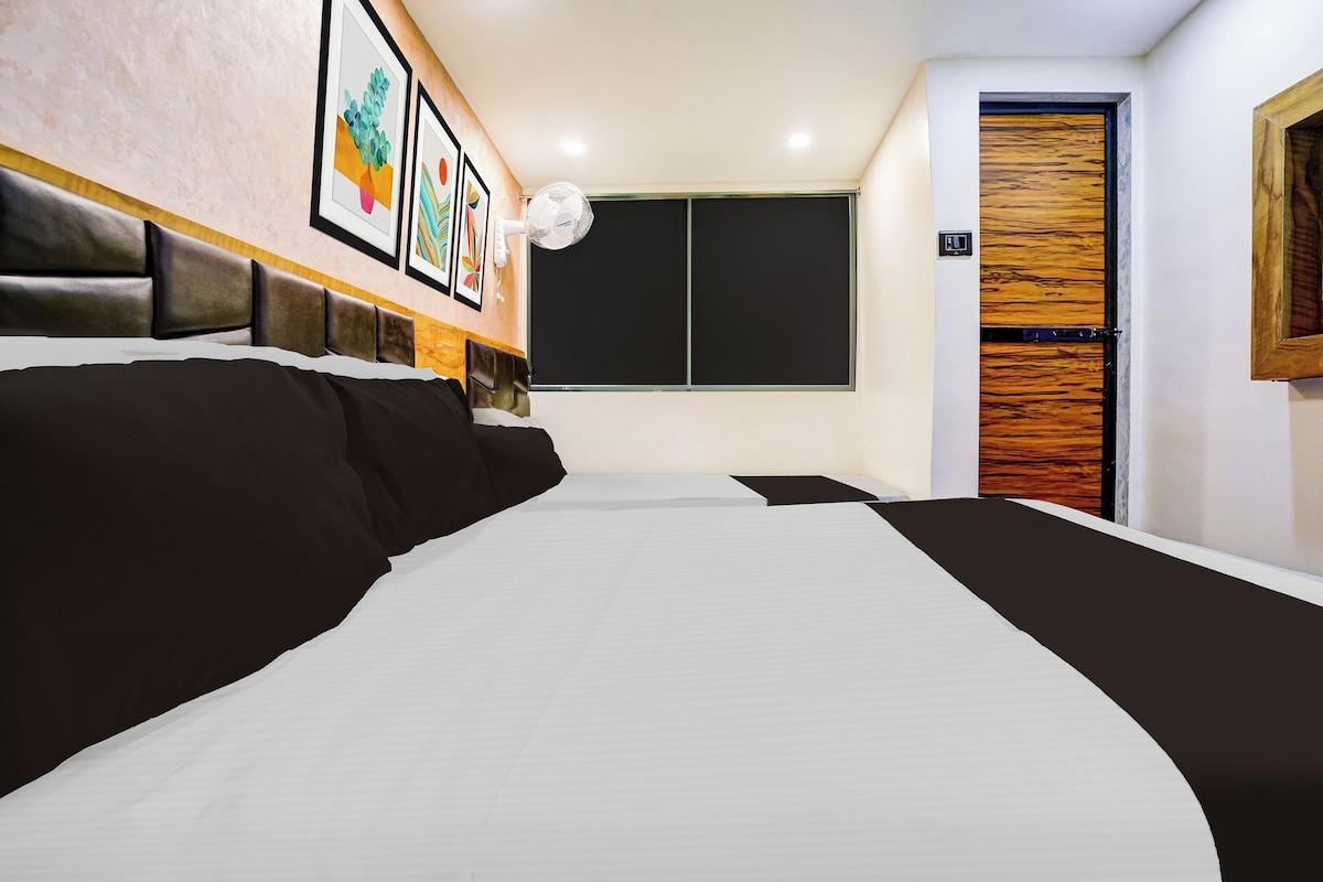 Ein Hotelzimmer mit einem großen Bett, einem Nachttisch, einem Wandventilator und einer Tür mit einem Holzpaneel.