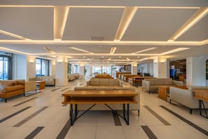 Eine geräumige Lobby mit einer zentralen Sitzecke, mehreren Sofas und einem langen Holztisch.