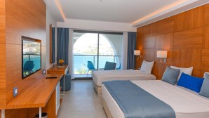 Ein Hotelzimmer mit zwei Betten, einem Schreibtisch, einem Fernseher und Blick aufs Meer.