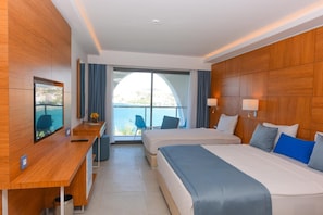 Ein Hotelzimmer mit zwei Betten, einem Schreibtisch, einem Fernseher und Blick aufs Meer.