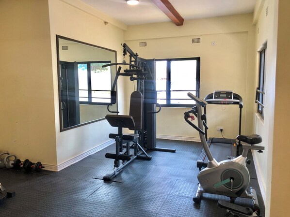 A gym with exercise equipment, a mirrored wall, and windows.