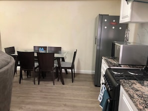A compact kitchen with a refrigerator, microwave, and stove. There is a dining table with chairs and a water bottle on it.