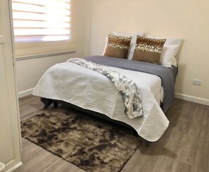 A bedroom with a bed, a fluffy rug, and a window with blinds. - Apartment in secure complex near Pamodzi Hotel (Lusaka)