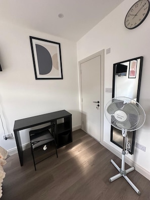A room with a black desk, a standing fan, a door, and a wall clock. - Apartment Sleeps 2 With Shared Kitchen Near City (London)