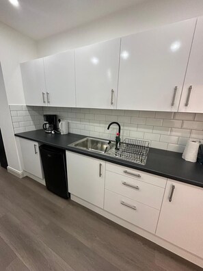 A modern kitchen with white cabinets, a black countertop, and a stainless steel sink. - Apartment Sleeps 2 With Shared Kitchen Near City (London)