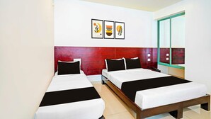 Ein Hotelzimmer mit zwei Einzelbetten, einem roten Kopfteil und drei gerahmten Kunstwerken an der Wand.