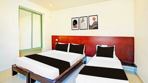 Ein Hotelzimmer mit zwei Betten, einem Holz-Kopfteil, einem großen Spiegel und drei gerahmten Kunstwerken an der Wand.