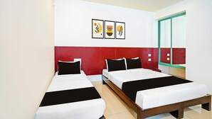 Ein Hotelzimmer mit zwei Betten, einer roten Akzentwand und drei gerahmten Kunstwerken über den Betten.