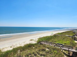Ein Strand mit einer Holzpromenade, die zum Ufer führt, bewölkter Himmel und ruhiges Meer.