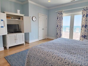 A bedroom with a bed, a TV, a wardrobe, a door, and a view of the beach. - Palmetto Cove - Oceanfront with Elevator and Awesome Deck (Pawleys Island)