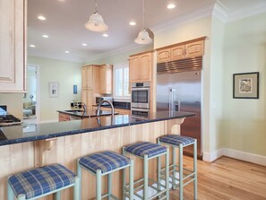 A kitchen with wooden cabinets, stainless steel appliances, a central island with bar stools, and pendant lighting. - Palmetto Cove - Oceanfront with Elevator and Awesome Deck (Pawleys Island)