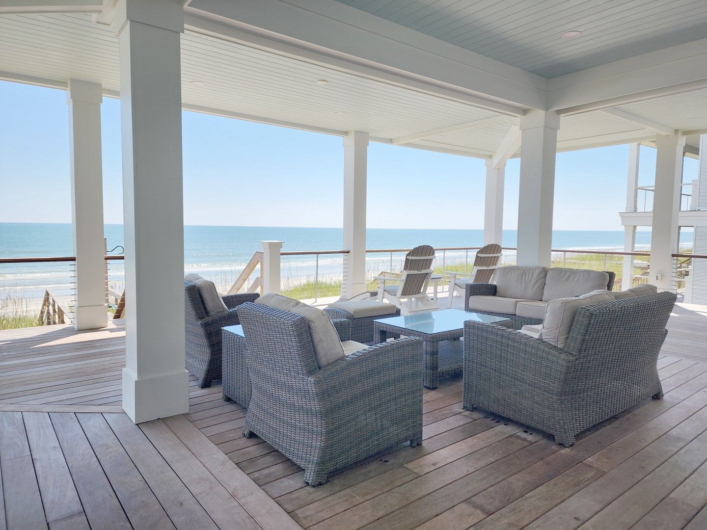 A covered outdoor seating area with wicker furniture and a glass table, overlooking a beach.