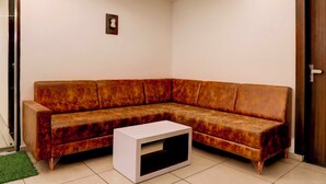 A corner living room with a brown sectional sofa, a white coffee table, and a door on the right. - Collection Ransan Circle Nana Chiloda (Gandhinagar)