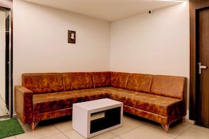 A corner living room with a brown sectional sofa, a white coffee table, and a door on the right. - Collection Ransan Circle Nana Chiloda (Gandhinagar)