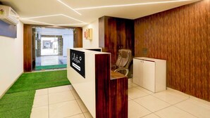 A reception area with a reception desk, a leather chair, a wooden wall panel, and a tiled floor. - Collection Ransan Circle Nana Chiloda (Gandhinagar)