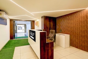 A reception area with a reception desk, a leather chair, a wooden wall panel, and a tiled floor. - Collection Ransan Circle Nana Chiloda (Gandhinagar)