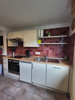 A compact kitchen with a stove, oven, sink, and white cabinets.