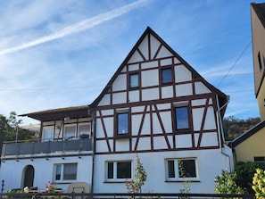 A two-story house with a steeply pitched roof, multiple windows, and a balcony.