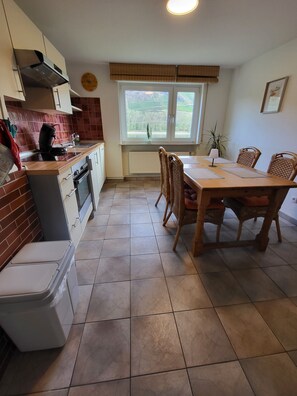 A kitchen with a dining table and chairs, a built-in oven, and a window with a view of greenery.