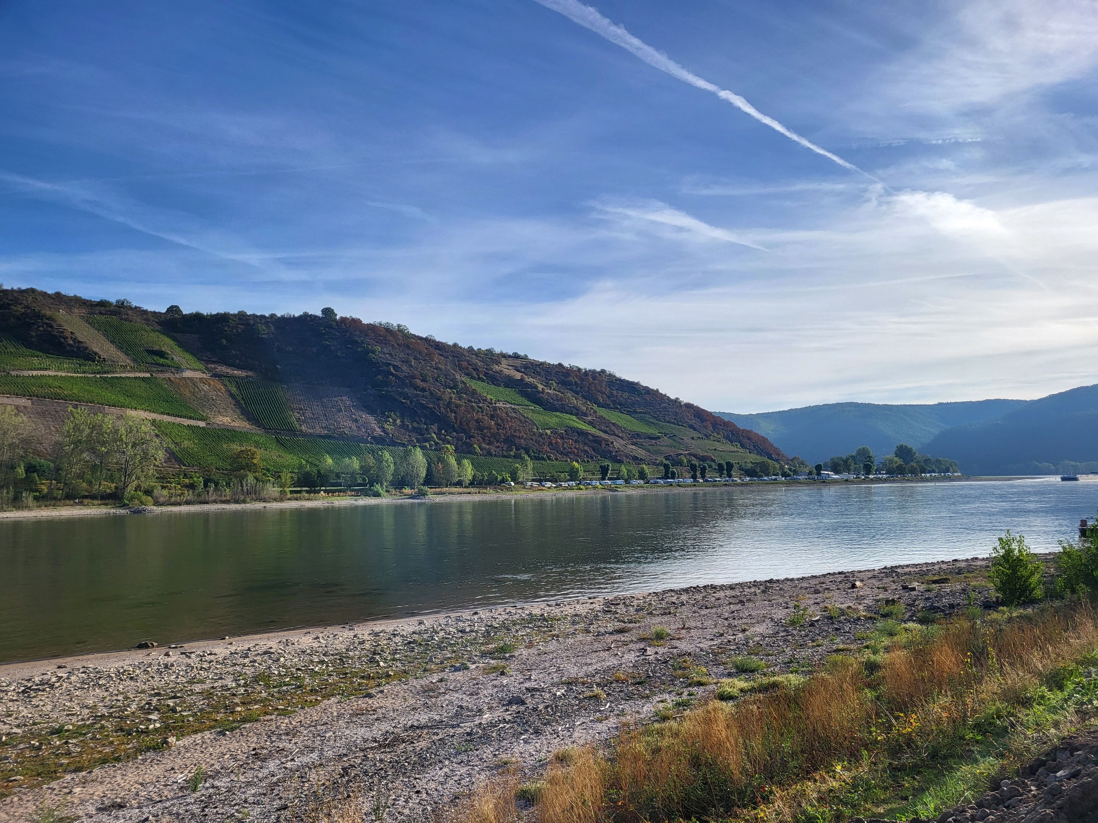 Ein Fluss mit steiniger Uferböschung und hügeliger Landschaft im Hintergrund.