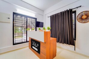 A reception area with a wooden desk, a blackboard sign, a TV mounted on the wall, and a window with a metal grill. - Collection O Kochi Mary Varkeys Park (Kanayannur)
