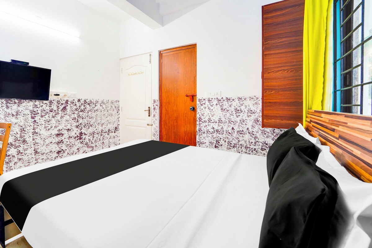 A hotel room with a bed, a TV, a wooden door, and a window with yellow curtains.