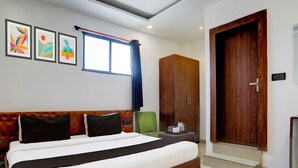 Quarto de hotel com cama, guarda-roupa, uma mesinha com chaleira e obra de arte na parede.
