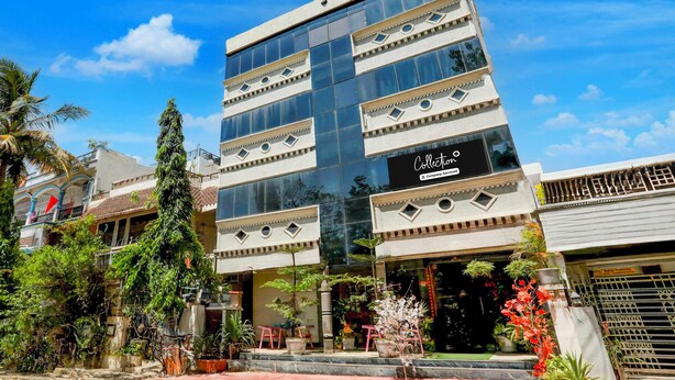 Um edifício moderno com fachada de vidro, uma placa com a inscrição 'Collection Company-Serviced' e um jardim bem cuidado com diversas plantas e áreas de estar.