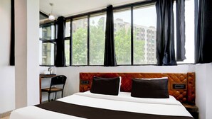 Quarto de hotel com uma cama grande, escrivaninha com cadeira e janela com cortinas.