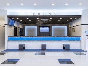 Een receptie met een 'FRONT' bordje, een digitaal scherm en een blauwe accentmuur.