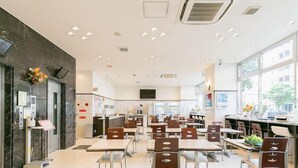 En modern restaurang med en stilren och rymlig inredning, med flera matbord och stolar, en bardisk och stora fönster som släpper in naturligt ljus.