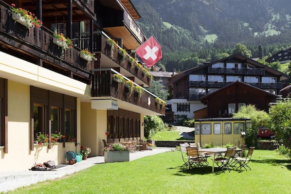 Un hotel con balcones decorados con flores, una bandera suiza y vistas a las montañas.