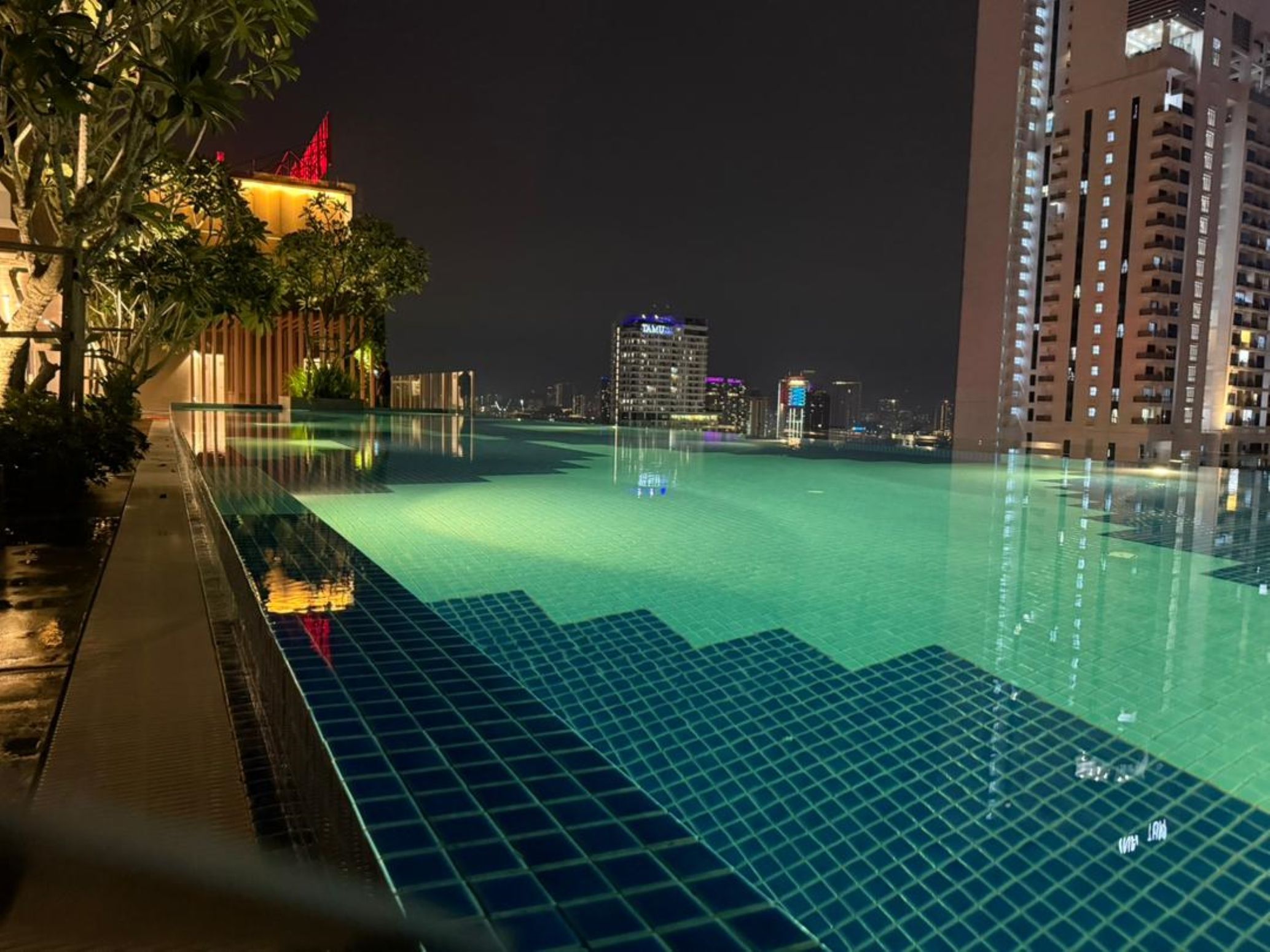 Vista nocturna de una piscina con un paisaje urbano al fondo.