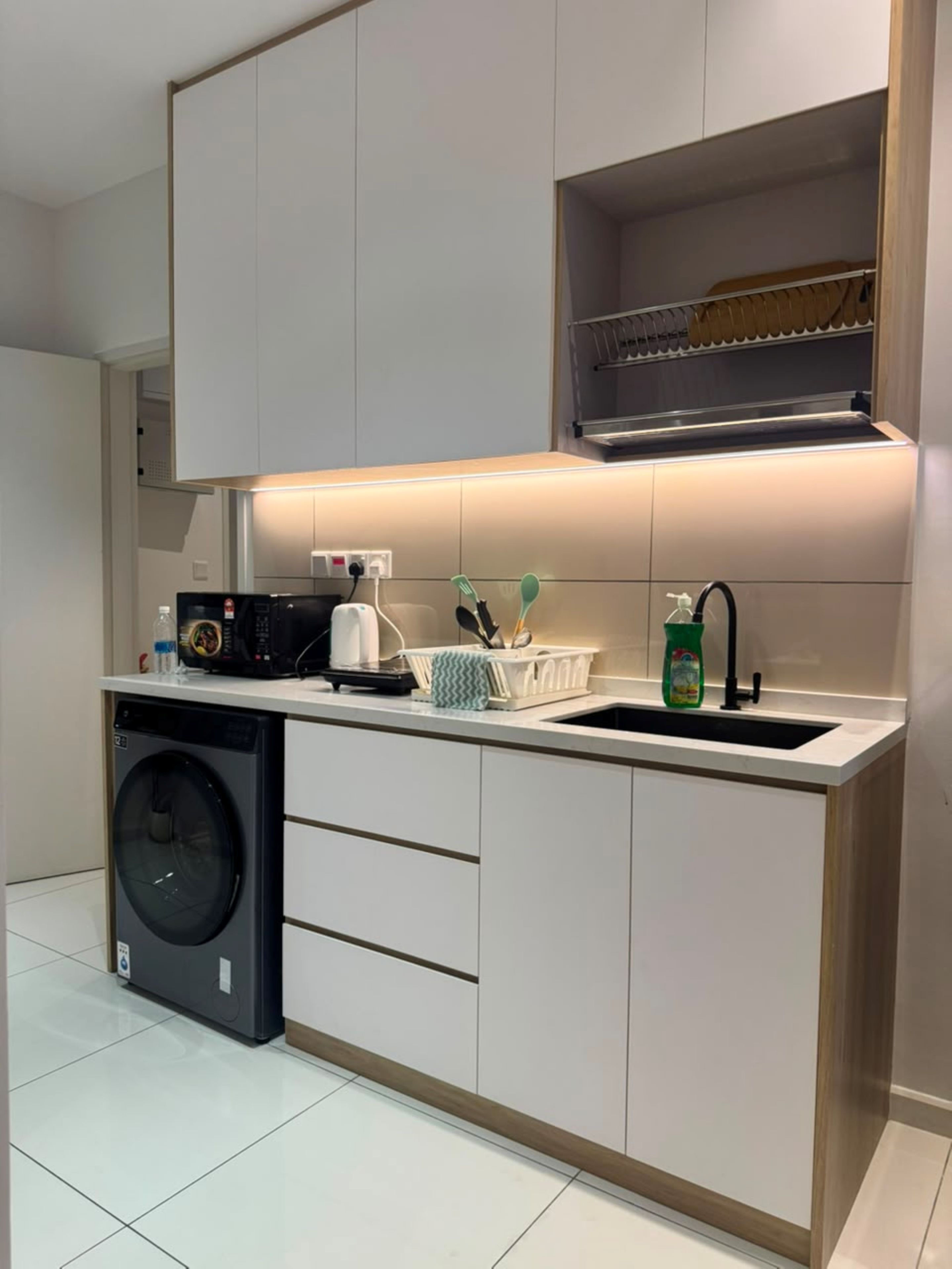 Cocina compacta con lavadora, pileta y encimera con diversos objetos.