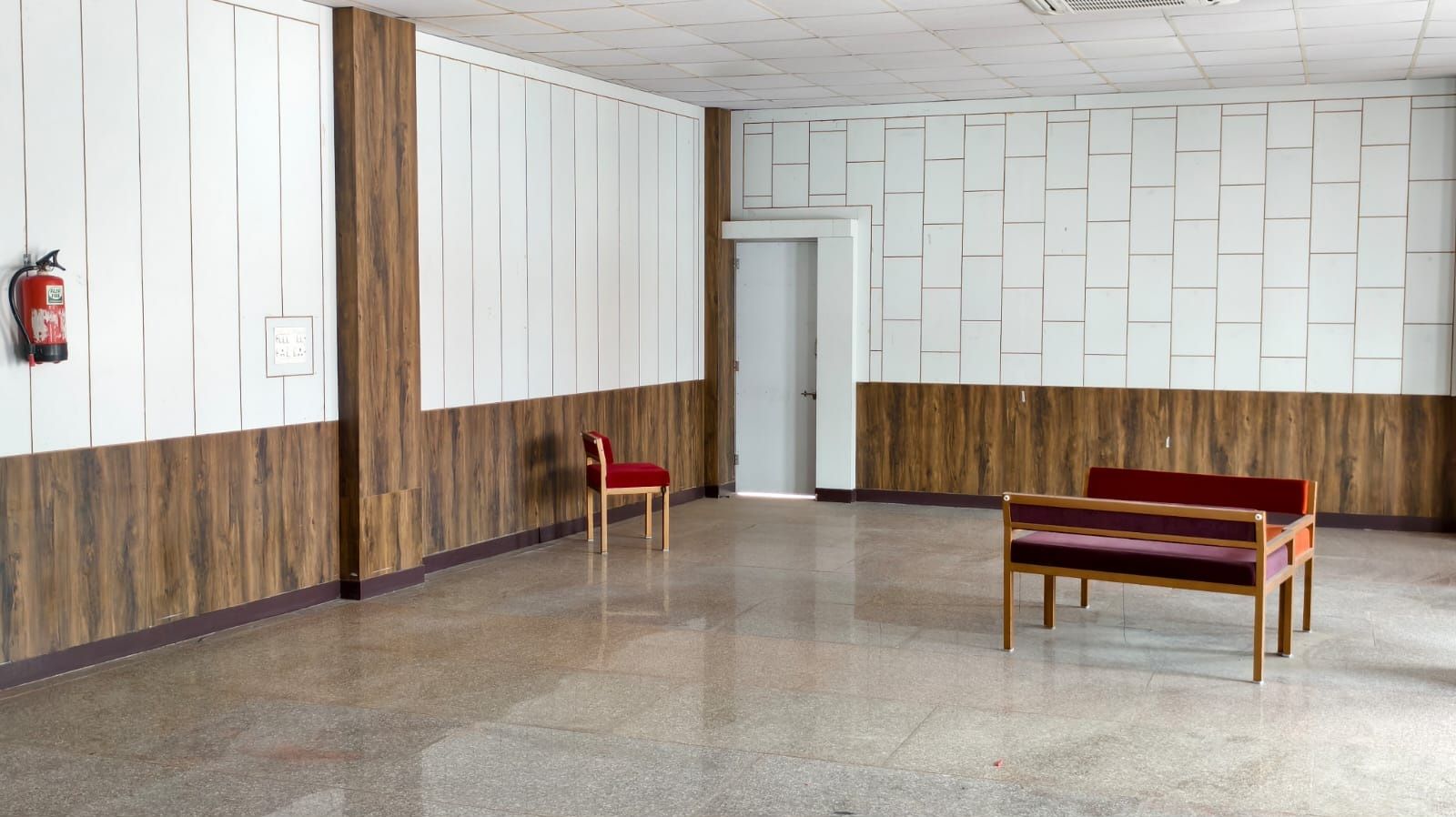 A hallway with a wooden panel wall, a fire extinguisher, a bench, and a door.