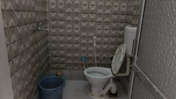Un baño pequeño y cerrado con un inodoro, un cubo azul y un lavabo de metal.