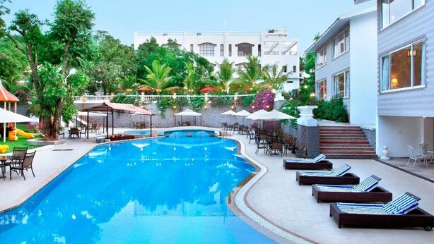 Una piscina con sillas de descanso, un área de estar techada y un edificio al fondo.