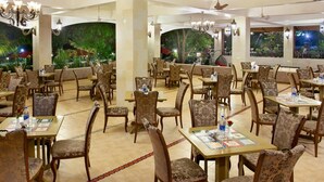 Un restaurante amplio con varias mesas y sillas, ventiladores de techo y un gran mural de una escena tropical.