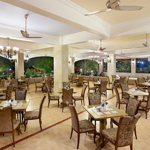 Un restaurant spacieux, doté de nombreuses tables et chaises, de ventilateurs de plafond et d’une grande fresque représentant un paysage tropical.