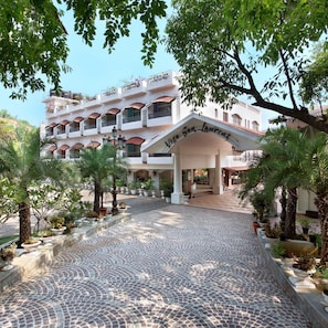 Una entrada de hotel con un camino de adoquines que conduce a un edificio blanco con balcones.