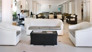 Un amplio espacio de sala con un sofá blanco, dos sillones, una mesa de centro y un comedor con sillas y una mesa.