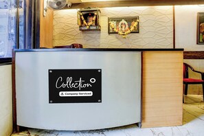 A reception desk with a 'Collection' sign, a wall-mounted fan, and a framed picture above the desk. - O Ulhasnagar Formerly Hotel Derby (Mumbai)