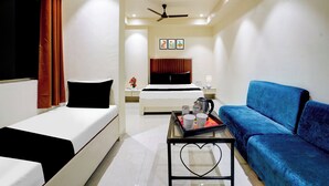 A hotel room with a bed, a blue sofa, a coffee table, and a ceiling fan. - O Ulhasnagar Formerly Hotel Derby (Mumbai)