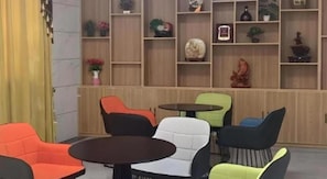 Ein Zimmer mit verschiedenen Sitzgelegenheiten, darunter Stühle und ein Tisch, eine Holzregaleinheit mit Dekorationen sowie ein Vorhang auf der linken Seite.